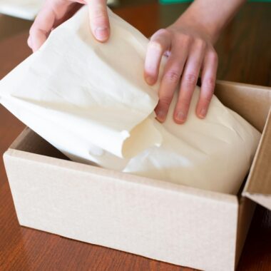 Hands wrapping merchandise in a cardboard box for shipping, ideal for small business stock images.